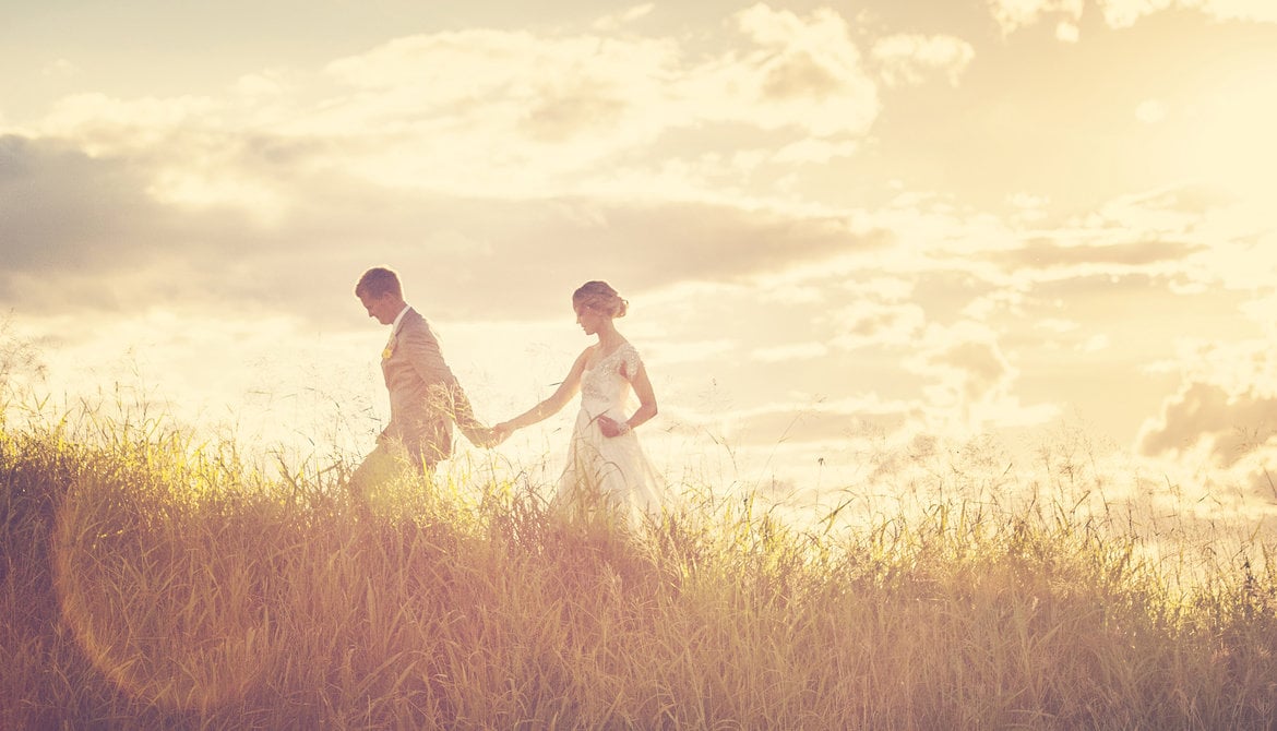 bride and groom walking through a field